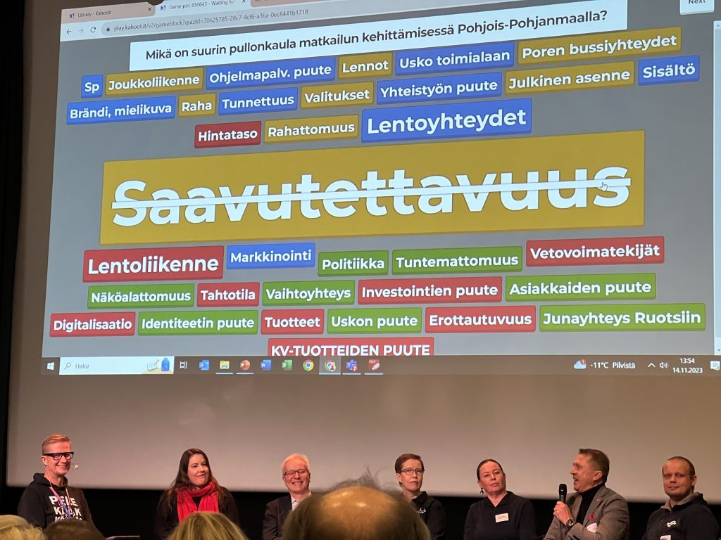 Sanoja heijastettuna näytölle, alapuolella paneelikeskustelijoita.