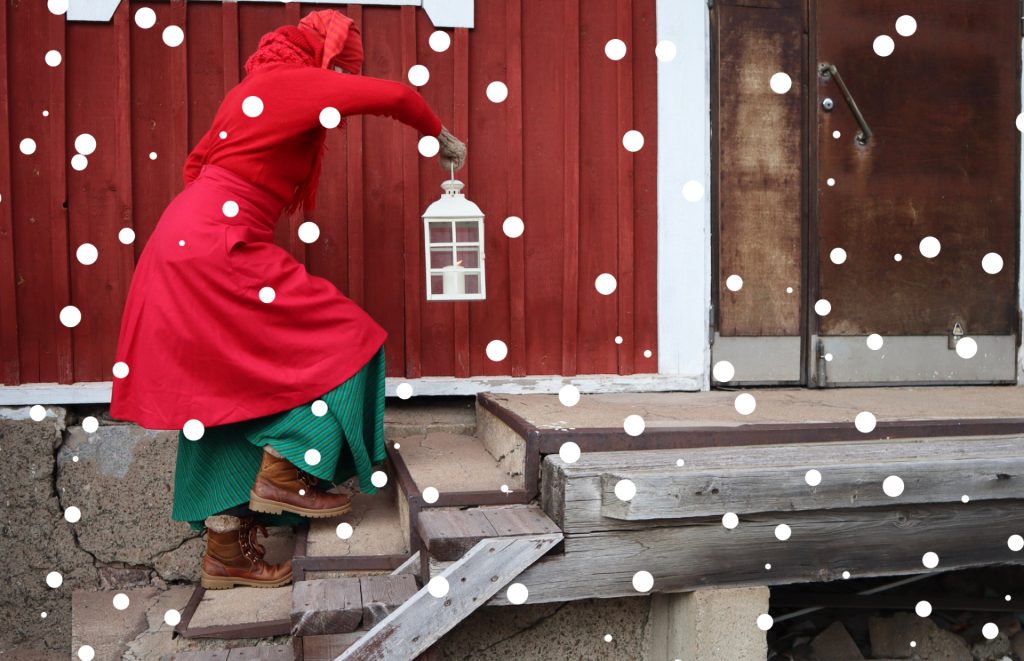 Tonttu kulkee portaissa käsissään kynttilälyhty. Tontulla on pitkä takki ja hame.