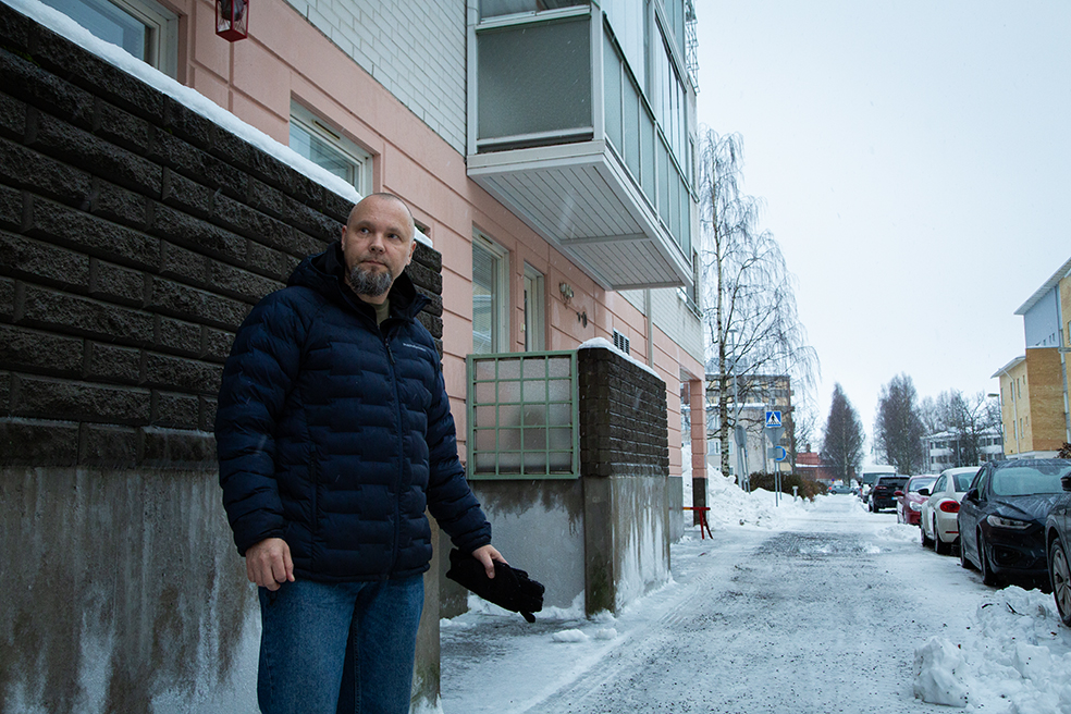 Mies seisoo kerrostalon edessä sohjoisella kadulla.