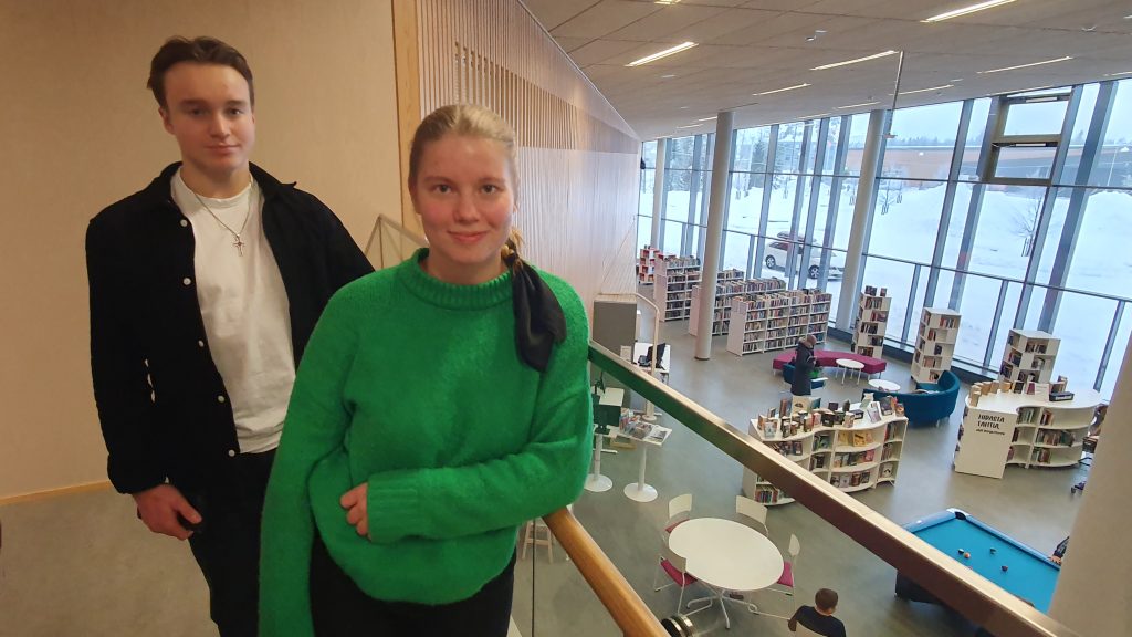 Nuoret henkilöt seisovat Hiukkavaaran monitoimitalon ylätasanteella. Taustalla näkyy kirjasto.