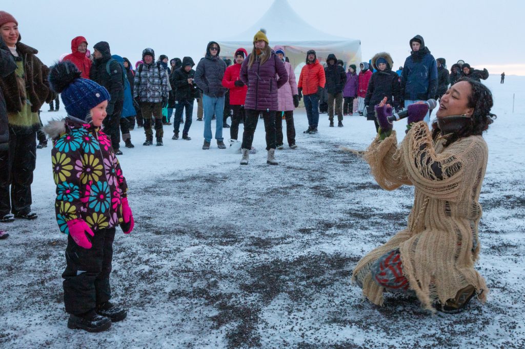 Nainen laulaa polvillaan yleisön edessä meren jäällä.