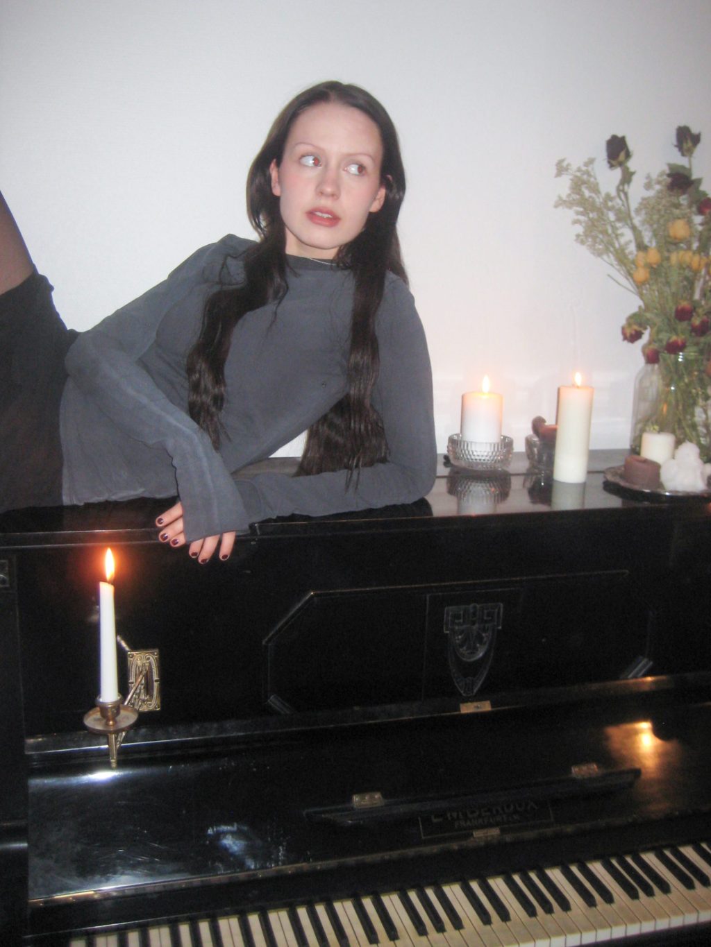 Nuori nainen nojaa pianoon, jonka päällä kynttilöitä.