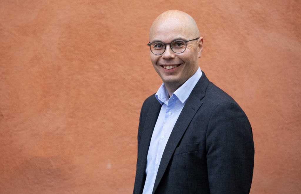 A bald man with glasses smiling for a camera.