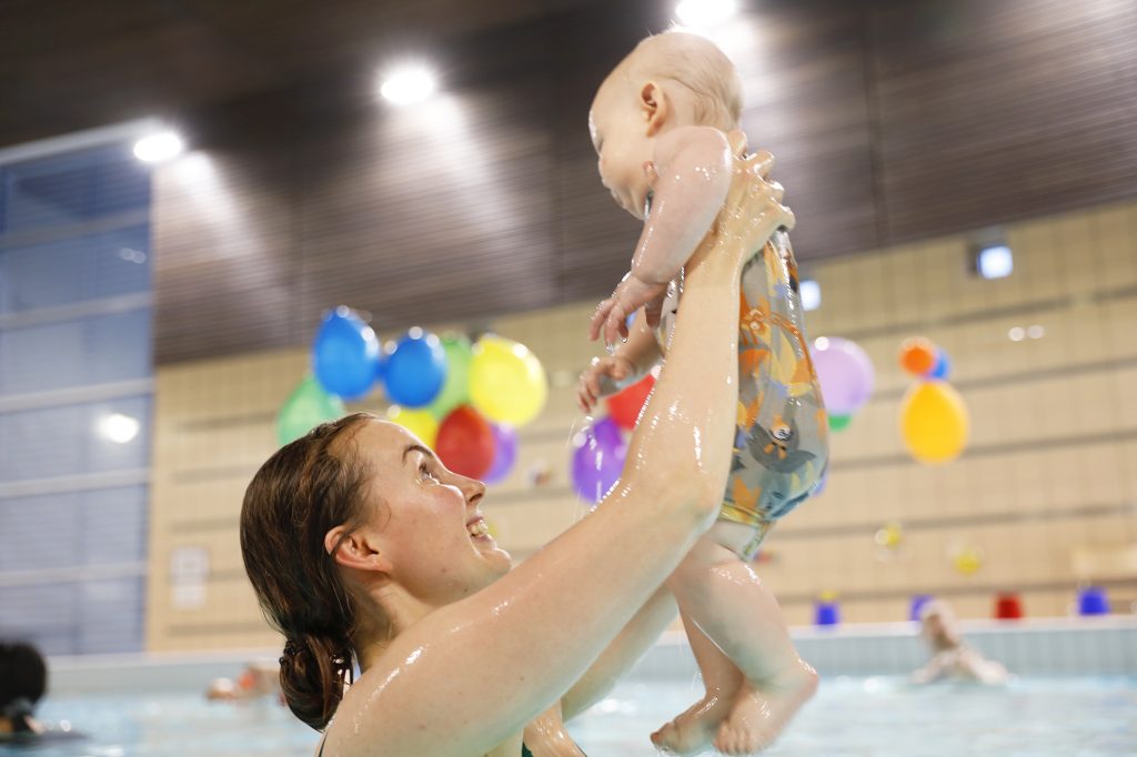 A mother holding a baby in a swimming pool.