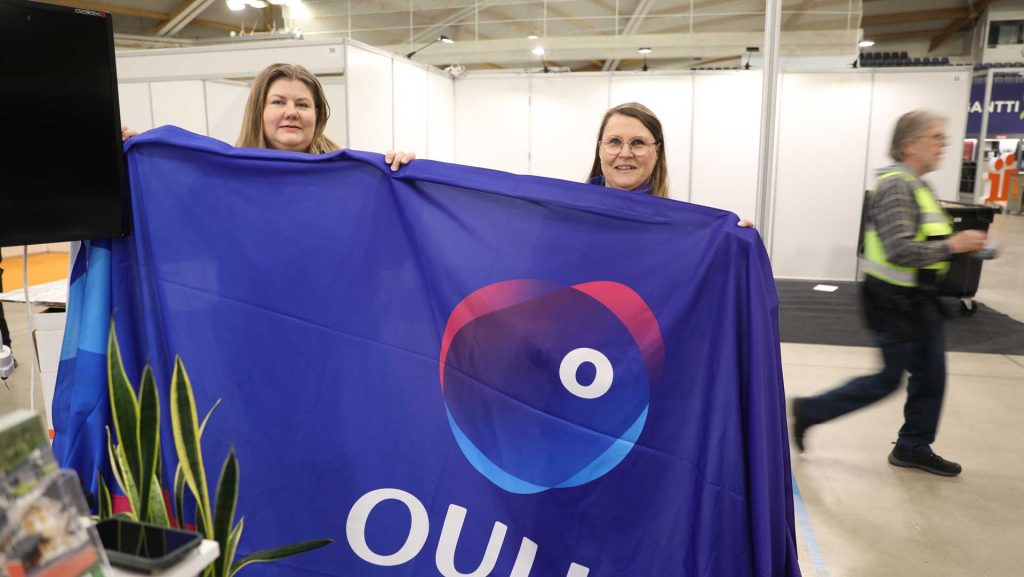 kaksi naista nostaa Oulu-logolippua ylös