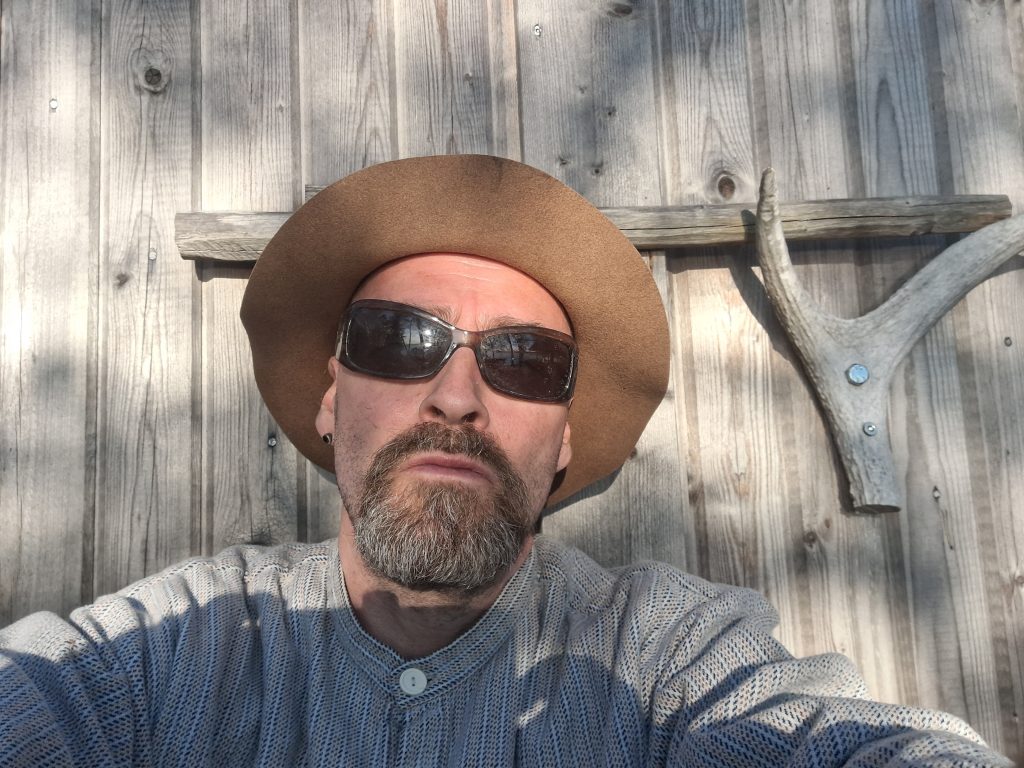 Mies hattu ja aurinkolasit päässä selfie-kuvassa.