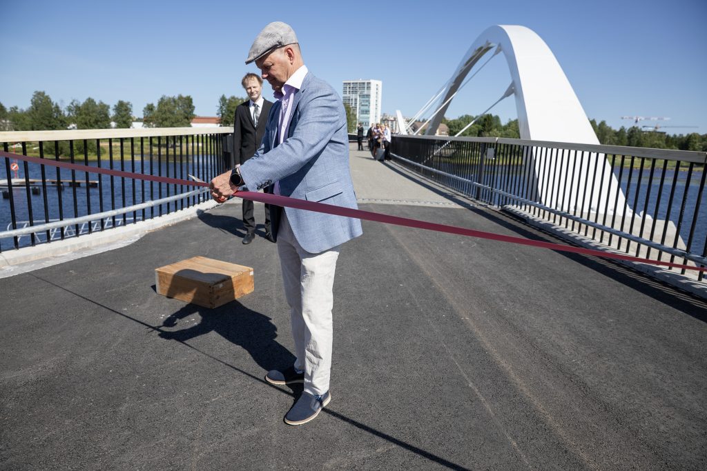 Lippalakkipäinen mies leikkaa nauhaa sillalla.