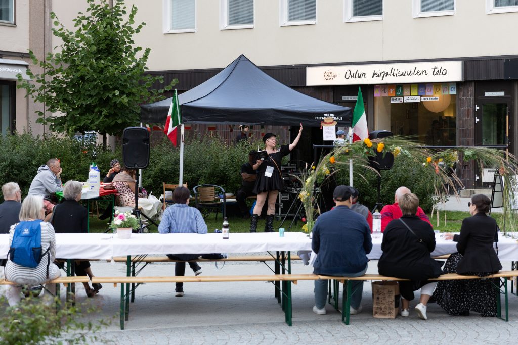 Runoilija esiintyy pienen telttakatoksen alla yleisön edessä.