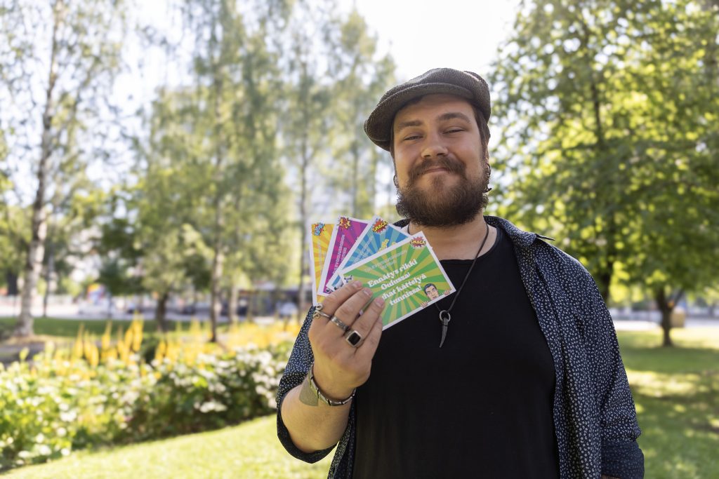 Mies puolilähikuvassa puistossa värikkäitä kortteja kädessään.