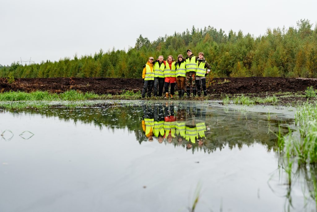 Ryhmä koululaisia poseeraa suolla, etualalla suolampi.