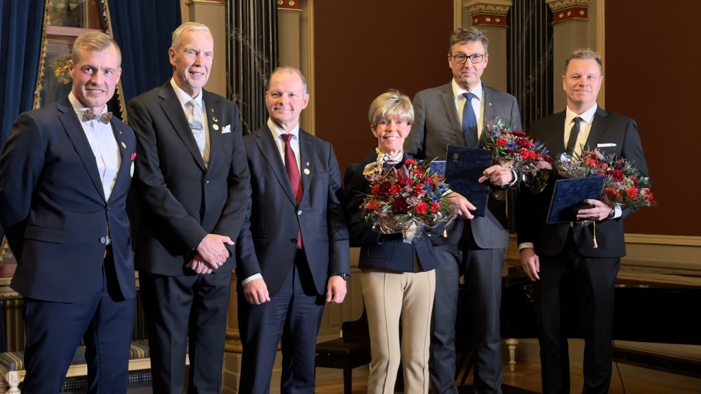 Viisi miestä ja yksi nainen ryhmäkuvassa juhlasalissa.