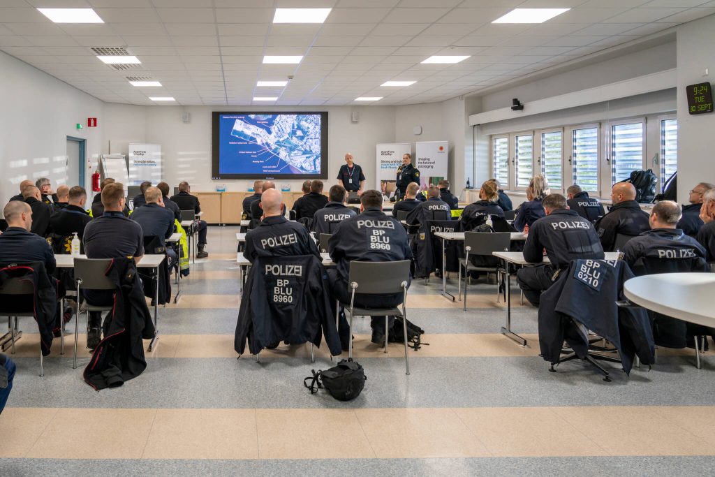 Poliiseja selin kokoustilaisuudessa. takkien selässä lukee Polizei.