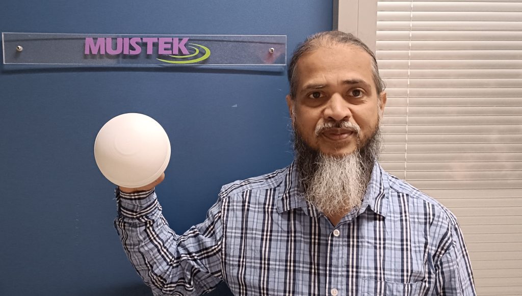 Parrakas mies poseeraa valkea pallonmuotoinen esine kädessään.