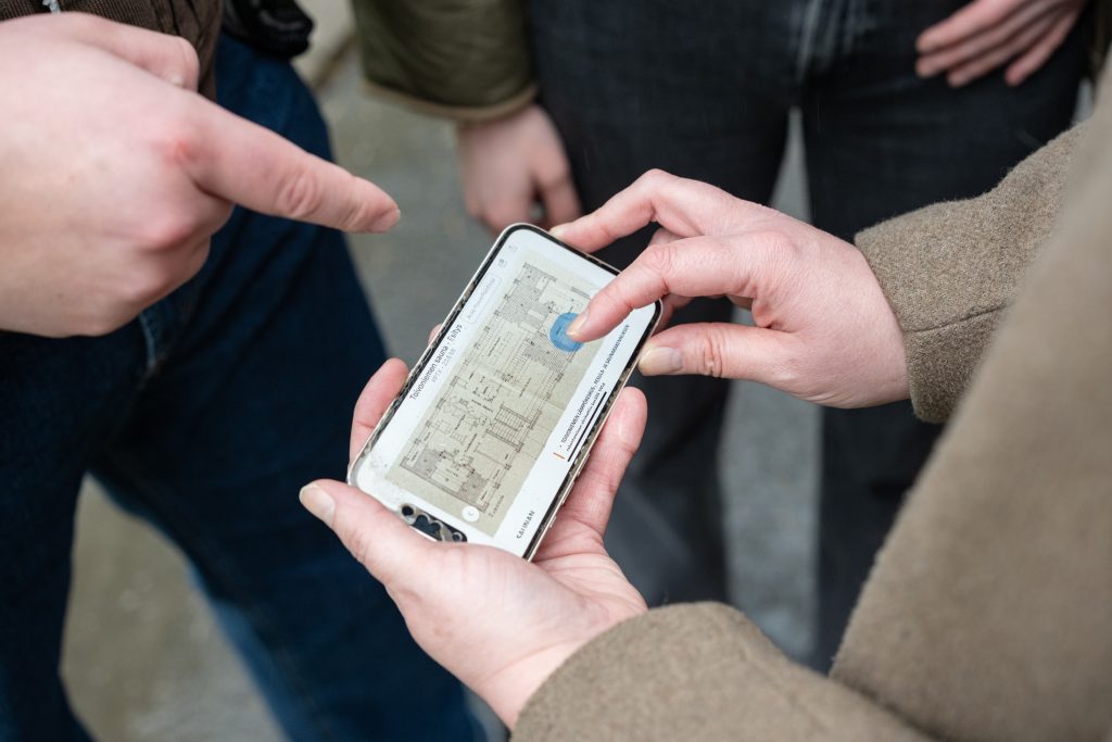 Lähikuva kännykkästä, jonka ympärillä usean ihmisen kädet.