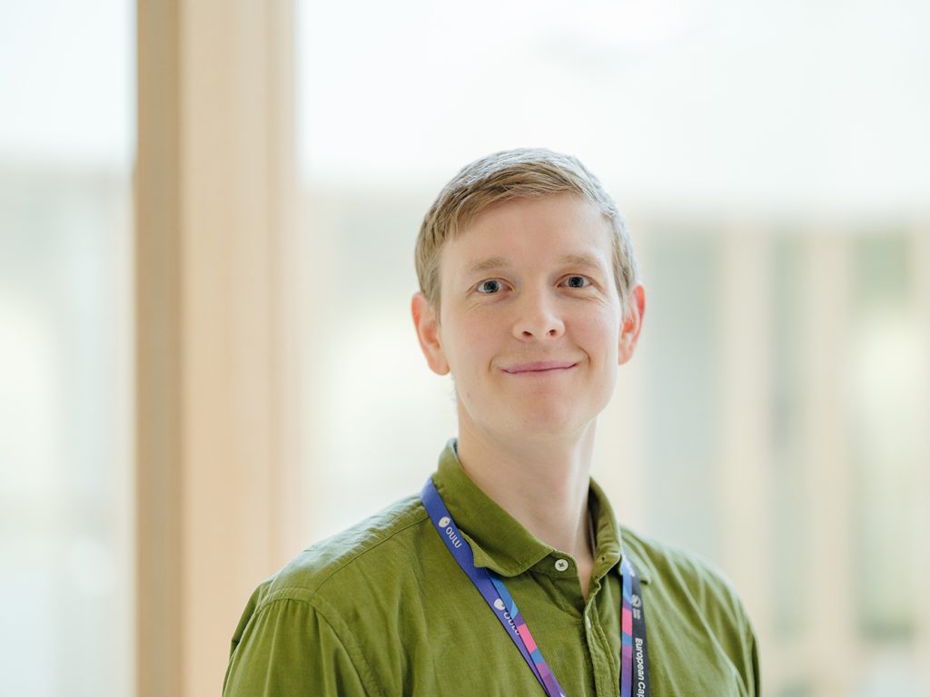 Nuori, vaalea mies vihreässä paidassa puolilähikuvassa