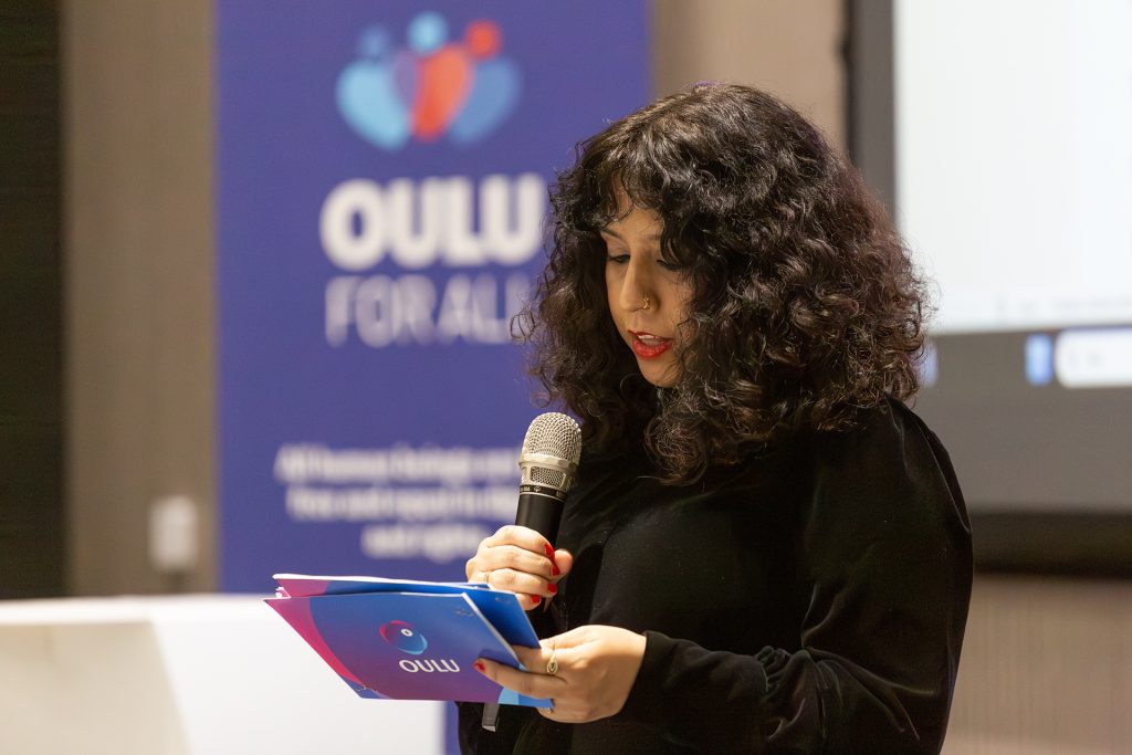 Tummahiuksinen nainen puhuu mikrofoniin.