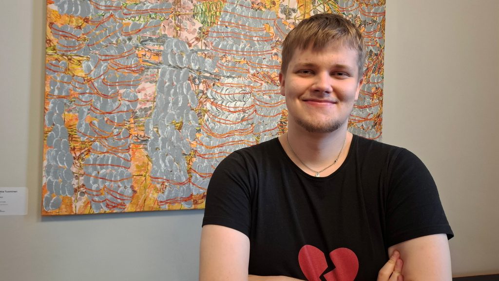 Nuori mies puolilähikuvassa abstraktin maalauksen edessä.