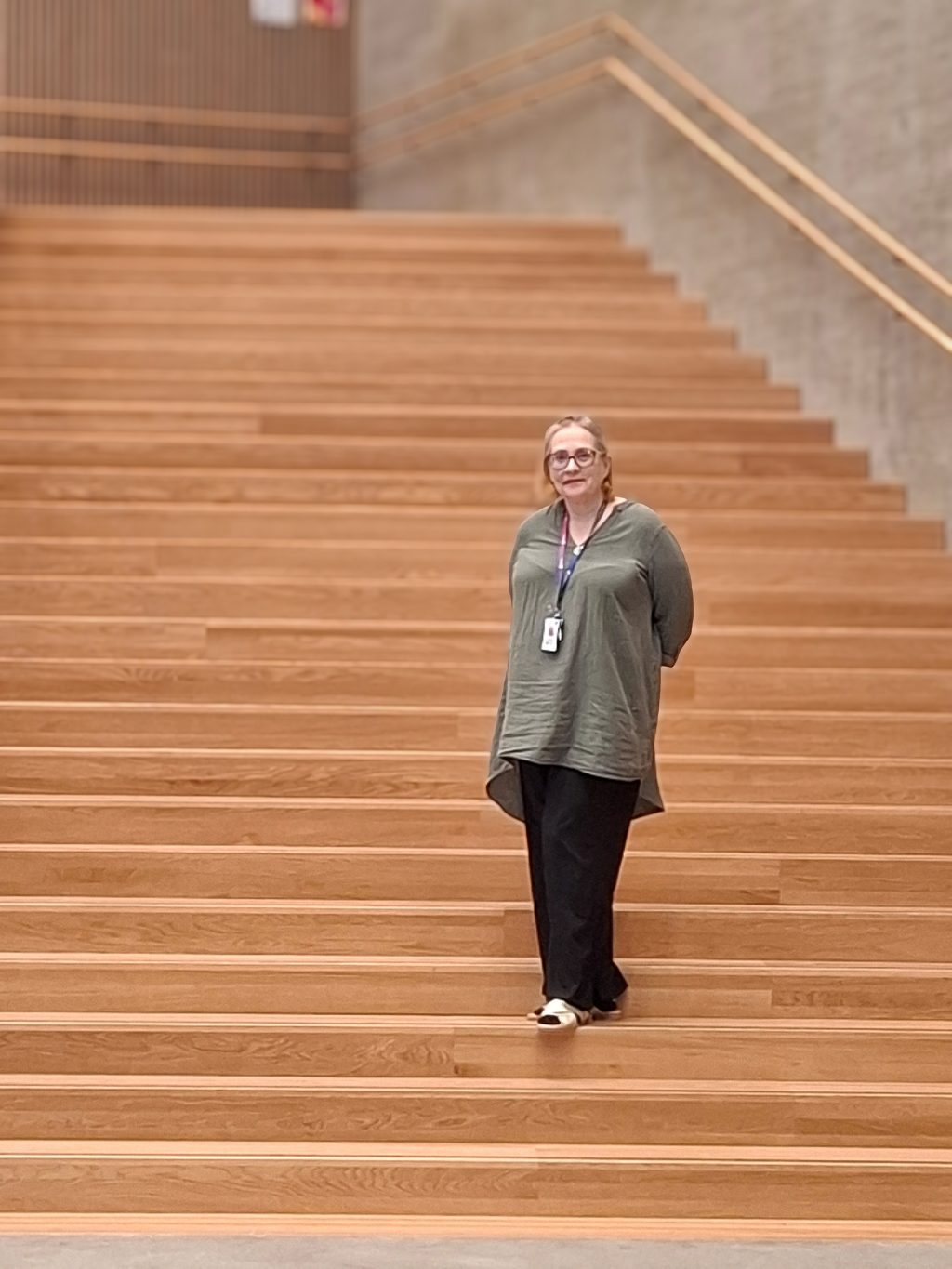 Vaalea, silmälasipäinen nainen poseeraa suurilla puuportailla.