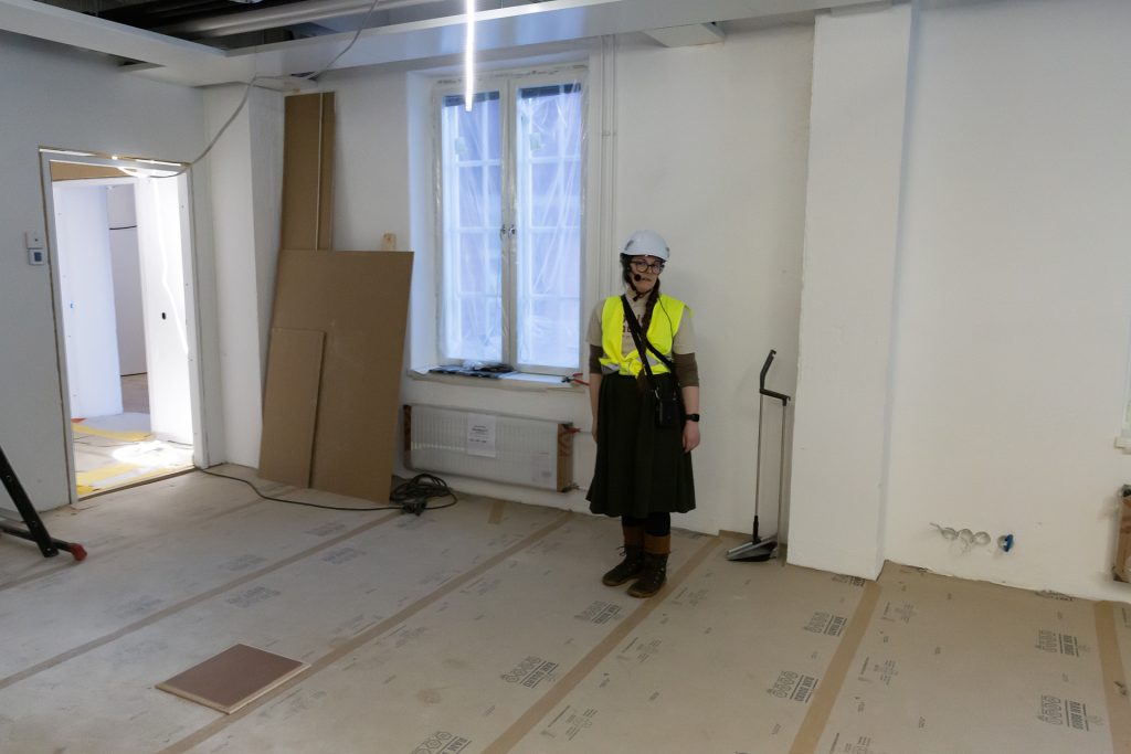 Nainen työmaavarusteissa tyhjässä tilassa.