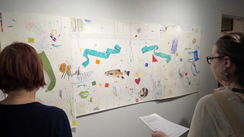 Kaksi naista tutkii kollaasimaista teosta seinällä.