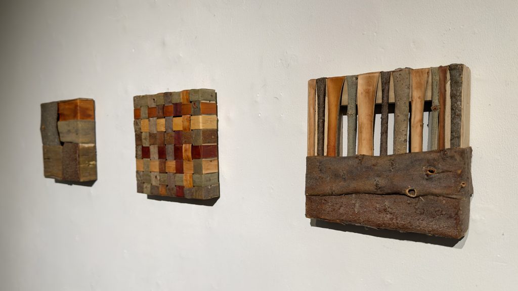 Kolme pientä puumateriaalista työstettyä taulua seinällä.