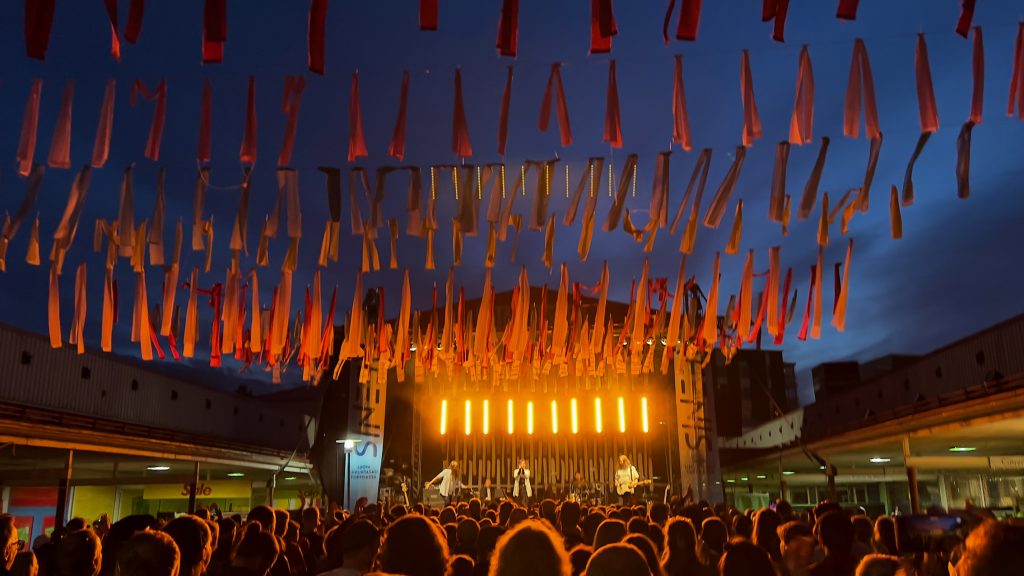 Yhtye esiintyy illan hämärtyessä festivaaliyleisön edessä, ilmassa roikkuu naruilta nauhoja.