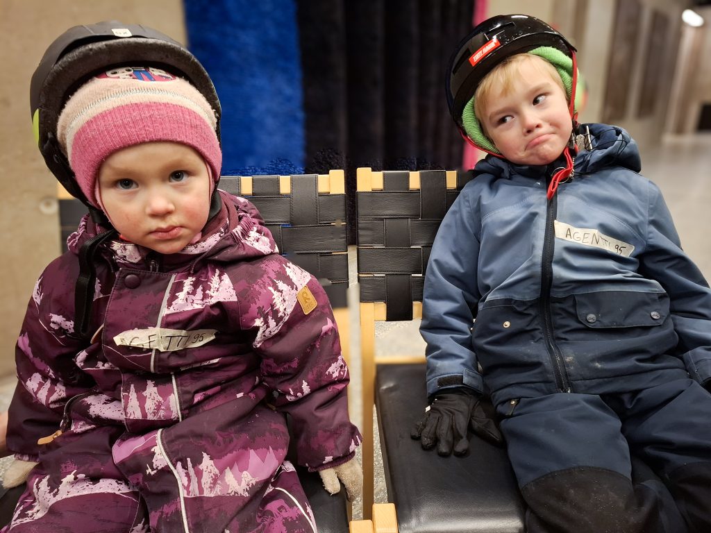 Kaksi pientä lasta istuu tuoleilla talvihaalareissa.