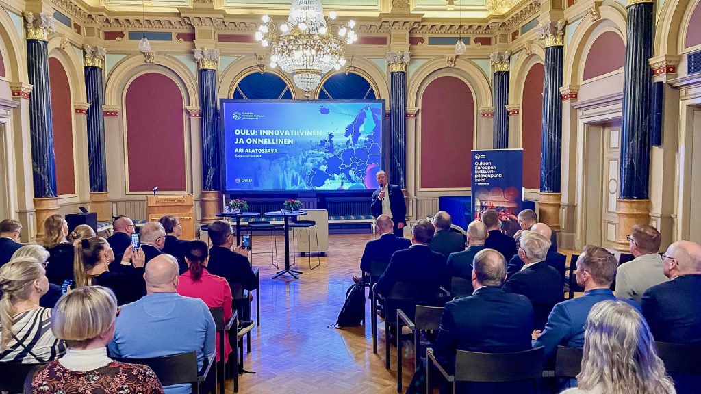 Ihmisiä juhlasalissa, kaupunginjohtaja pitää puhetta.