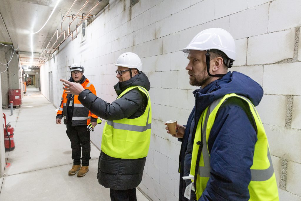 Kolme miestä työmaavarusteissa rakenteilla olevalla käytävällä.