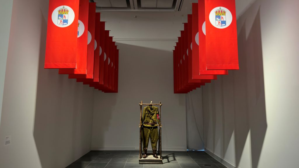 Taideinstallaatio, jossa lippuja ja sotilaspuku.