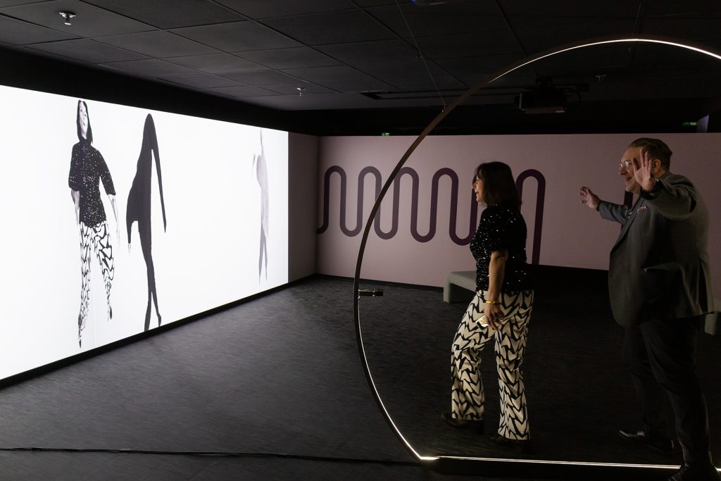 Nainen ja mies liikkuvat interaktiivisessa taideteoksessa, jossa heidän vääristyneet kuvansa heijastuvat seinälle.