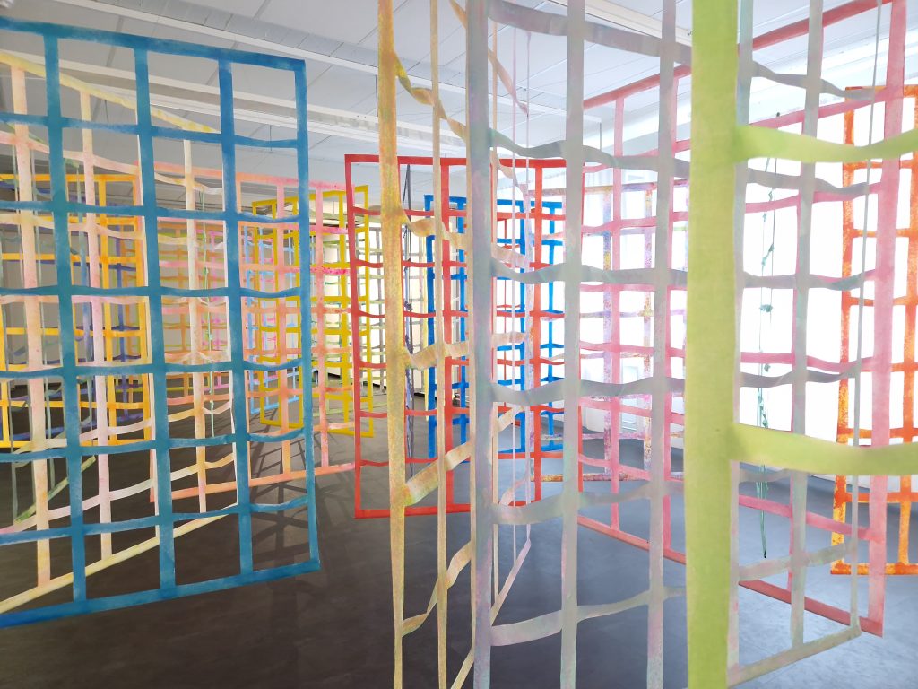 Tekstiilitaideteos, jossa suuria ruudukkomaisia kehikoita huoneessa.