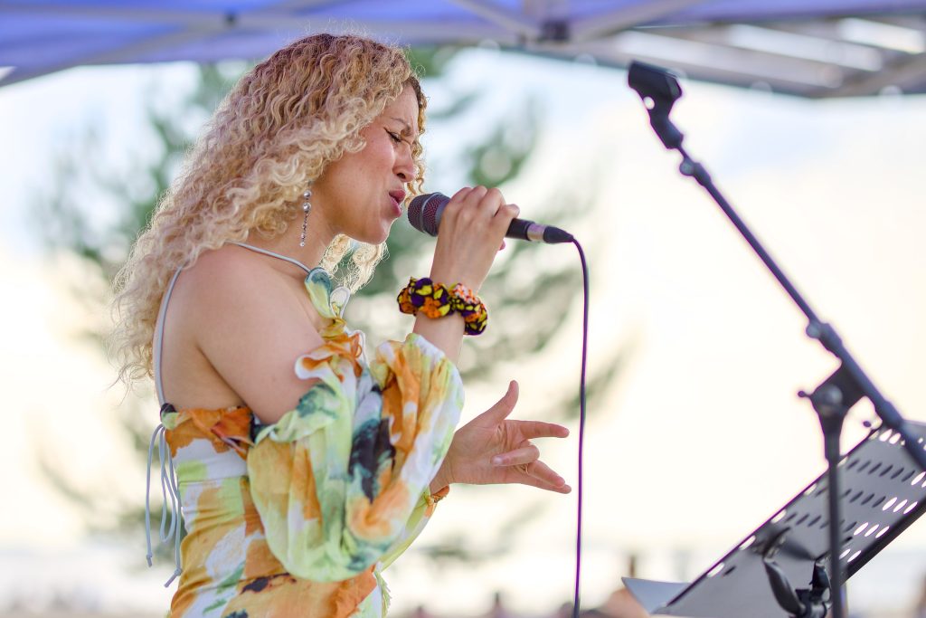 Vaaleahiuksinen laulaja värikkäässä mekossa puolilähikuvassa sivuprofiilissa.