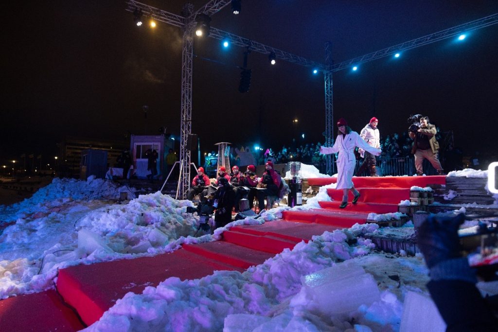 Kylpytakkiin pukeutunut ihminen kävelee lumen reunustamalla punaisella matolla.