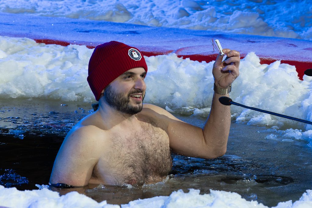 Pipopäinen, parrakas mies puhuu avannossa pieni laite kädessään.