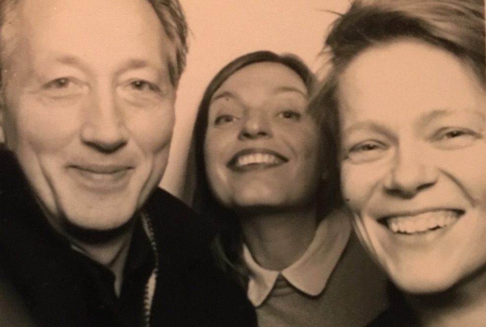 Mies ja kaksi naista hymyilevät seepianväriseksi sävytetyssä lähikuvassa.