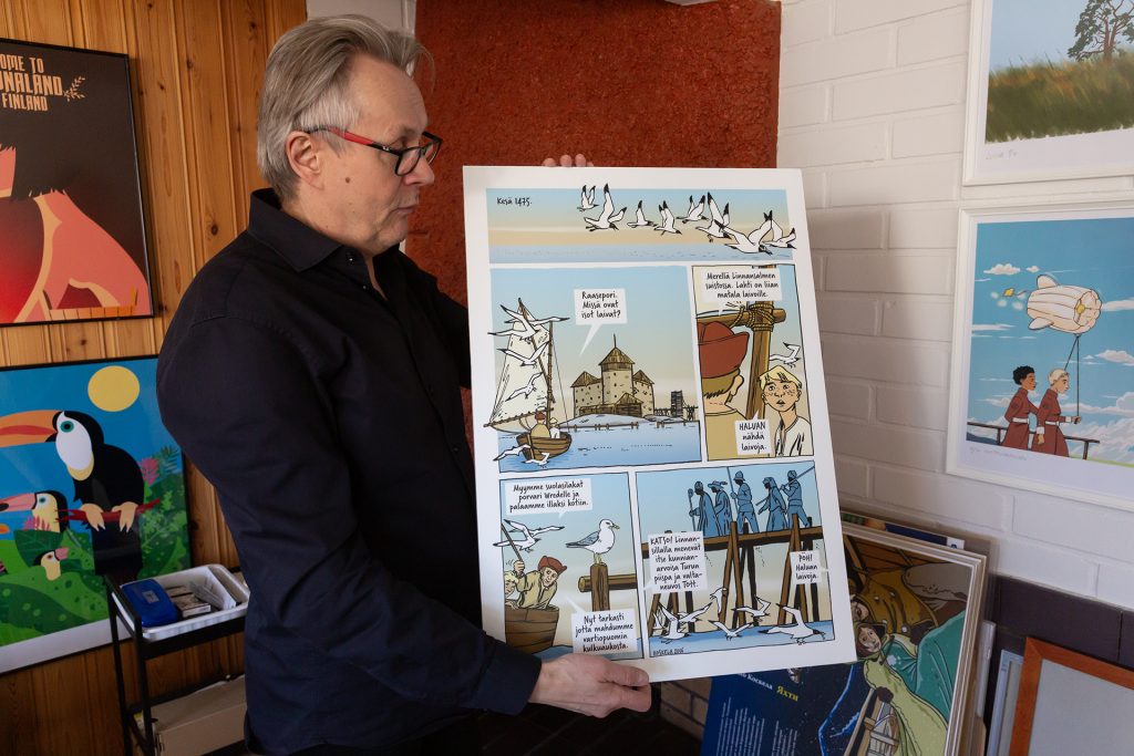 Silmälasipäinen mies käsissään julistekokoinen vedos sarjakuvasivusta.