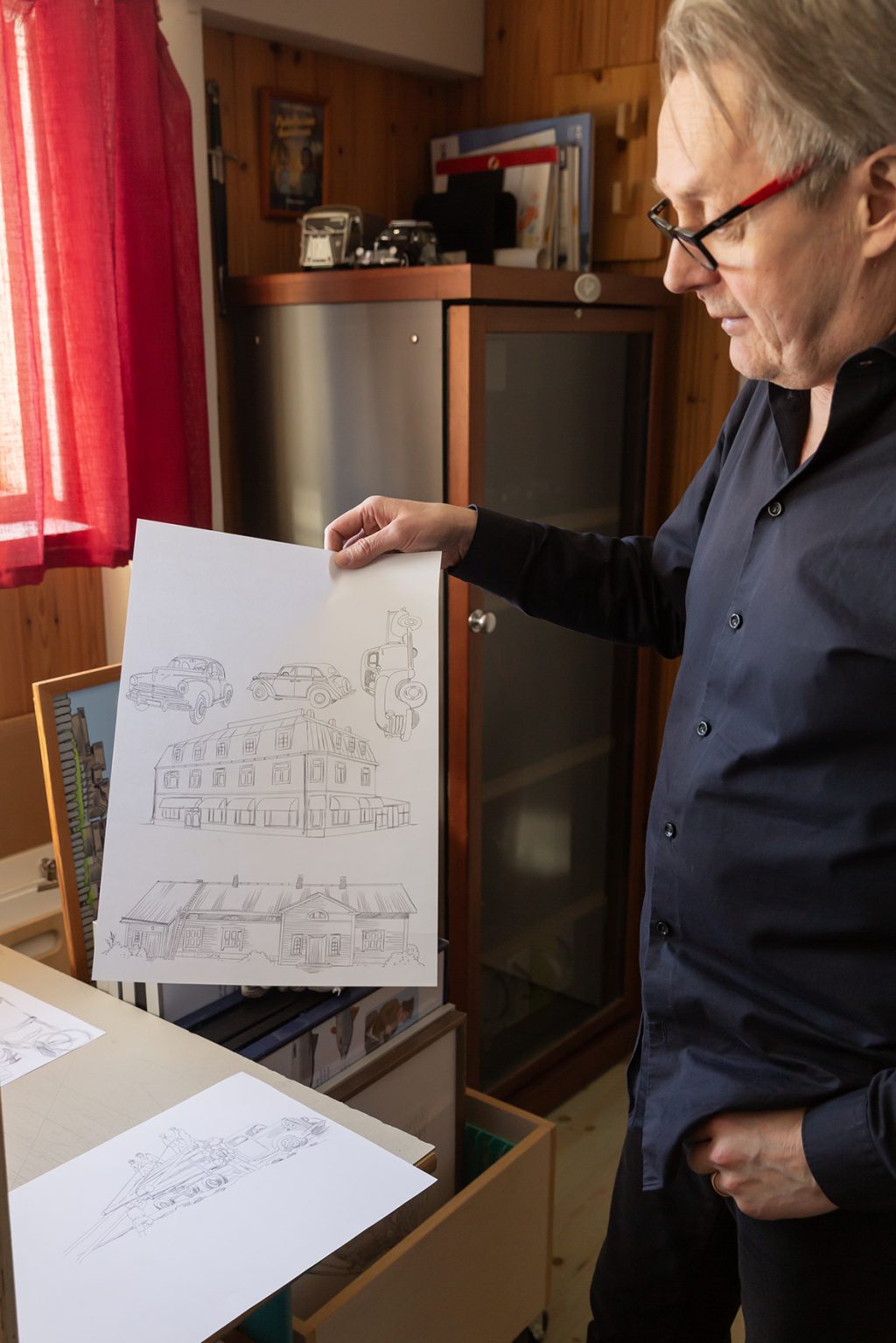 Mies pitelee paperia, jossa lyijykynäpiirroksia taloista ja autoista.