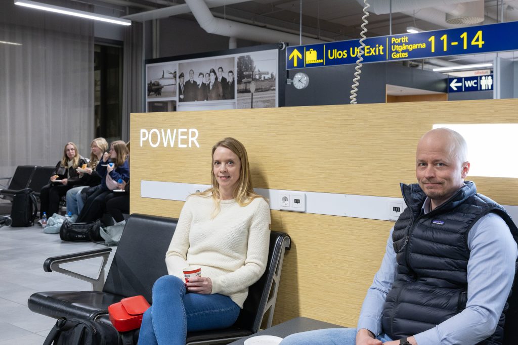 Pariskunta istuu lentokentän lähtöaulan tuoleilla.