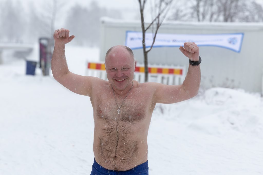 Kalju mies ylävartalo paljaana tuulettaa lumisessa maisemassa.