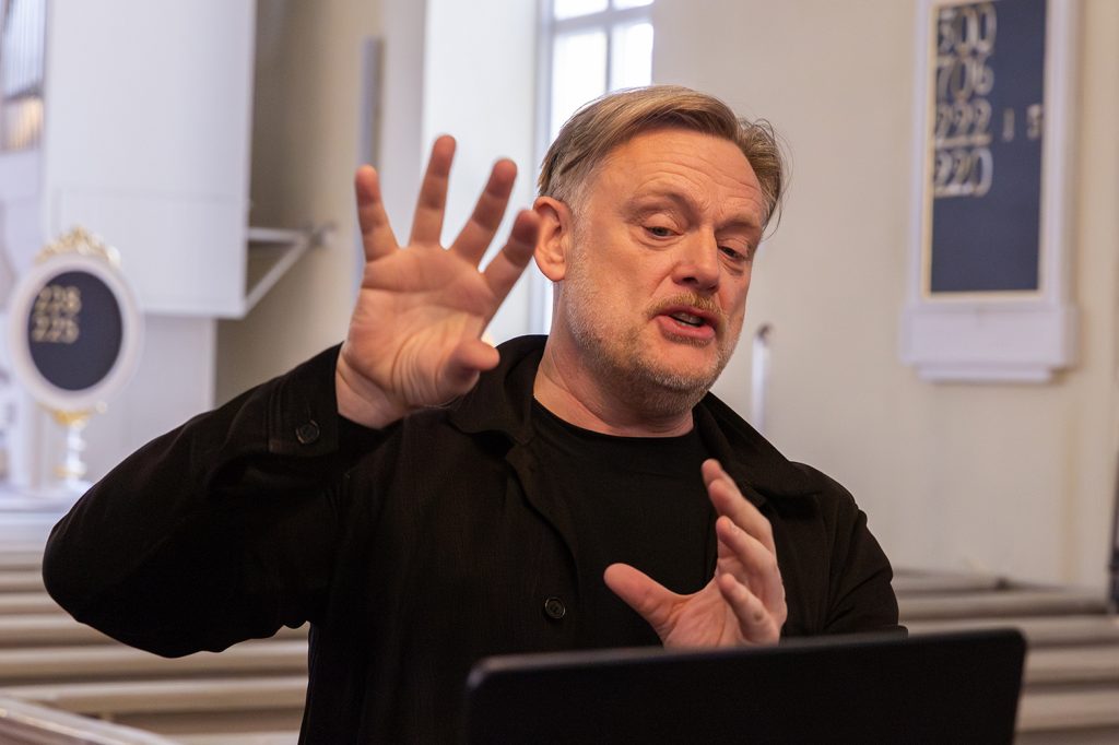 Mies puhuu kädet ilmassa edessään kirkkosalissa.