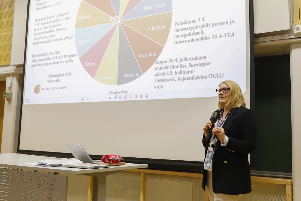 Nainen puhuu valkokankaan edessä.