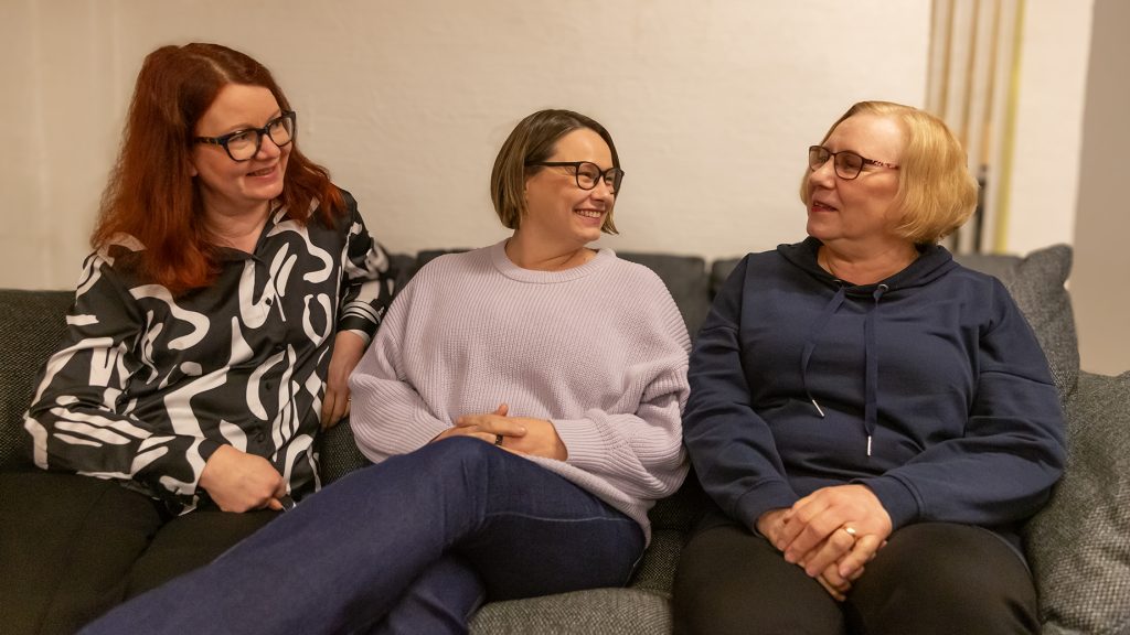 Kolme naista katsoo toisiaan ja nauraa sohvalla.
