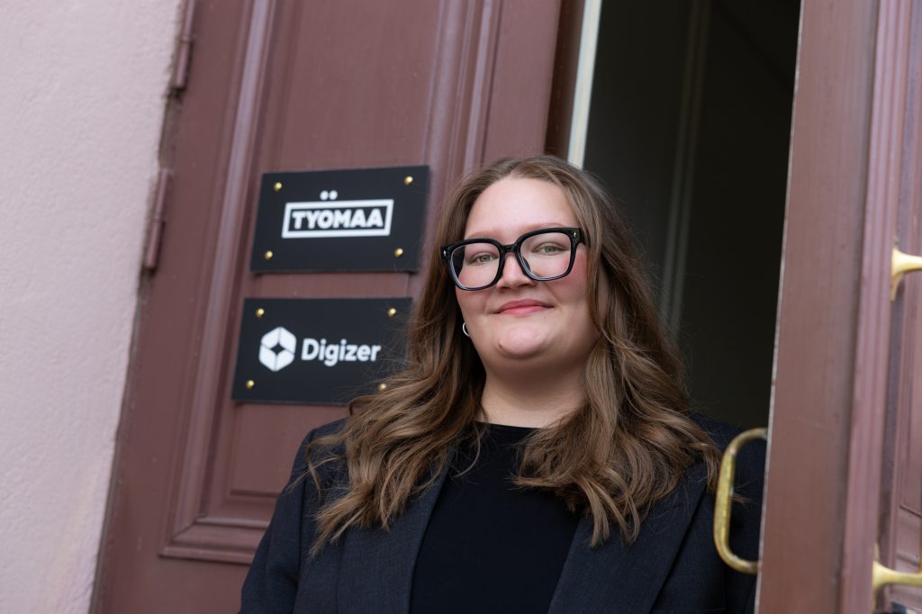 Silmälasipäinen nuori nainen poseeraa rakennuksen oviaukossa.