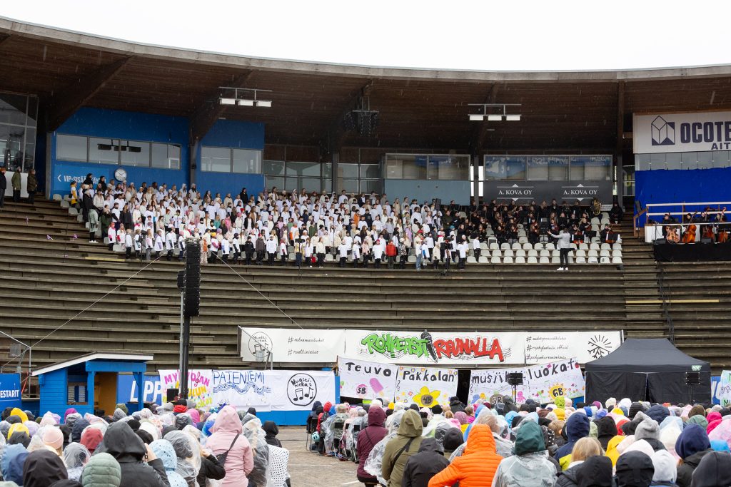 Kuoro stadionin katsomossa, etualalla yleisöä.