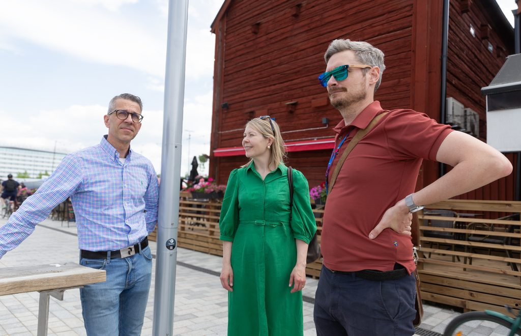 Kaksi miestä ja nainen seisovat punaisen aitan edustalla.