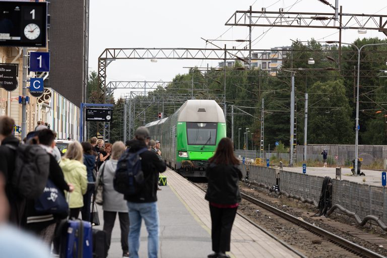 Juna saapuu asemalle, ihmisiä odottaa asemalaiturilla.