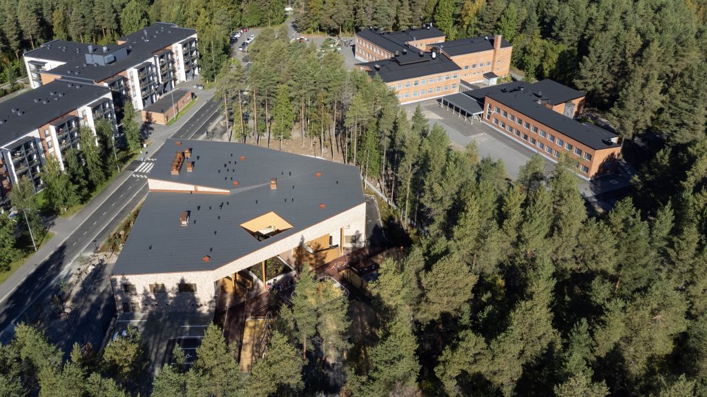 Ilmakuva metsän keskellä olevasta monitoimitalosta ja koulurakennuksesta.