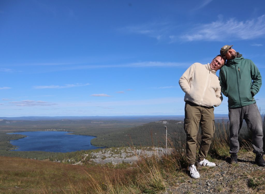 Kaksi miestä poseeraa toisiinsa nojaten tunturin laella.