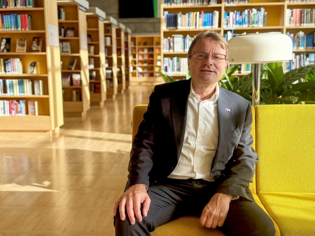 Mies istuu kirjastosalissa keltaisella sohvalla.